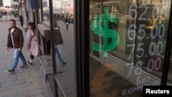 FILE - People walk past an exchange office screen showing the currency exchange rates, in Moscow, Russia, April 10, 2018. 