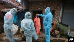 A health worker wearing personal protective equipment checks the temperature of a woman at a slum in Mumbai, India, June 17, 2020. 