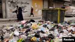 বিদ্রোহীরা উত্তরাঞ্চলীয় প্রধান শহর আলেপ্পো দখল করার পর আবর্জনার স্তূপের পাশ দিয়ে নারীরা হেঁটে যাচ্ছেন। ৪ ডিসেম্বর, ২০২৪।