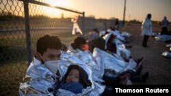 Dustin, an asylum-seeking migrant from Honduras, holds his son Jerrardo, 6, as they awake at sunrise next to others who took refuge near a baseball field after crossing the Rio Grande river into the US from Mexico, in La Joya, Texas, March 19, 2021.