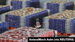 Seorang pekerja memakai masker pelindung saat menyusun tumpukan karung berisi beras, di tengah wabah Covid-19 di Surabaya, Jawa Timur, 20 April 2020. (Foto: Antara/Moch Asim via REUTERS)