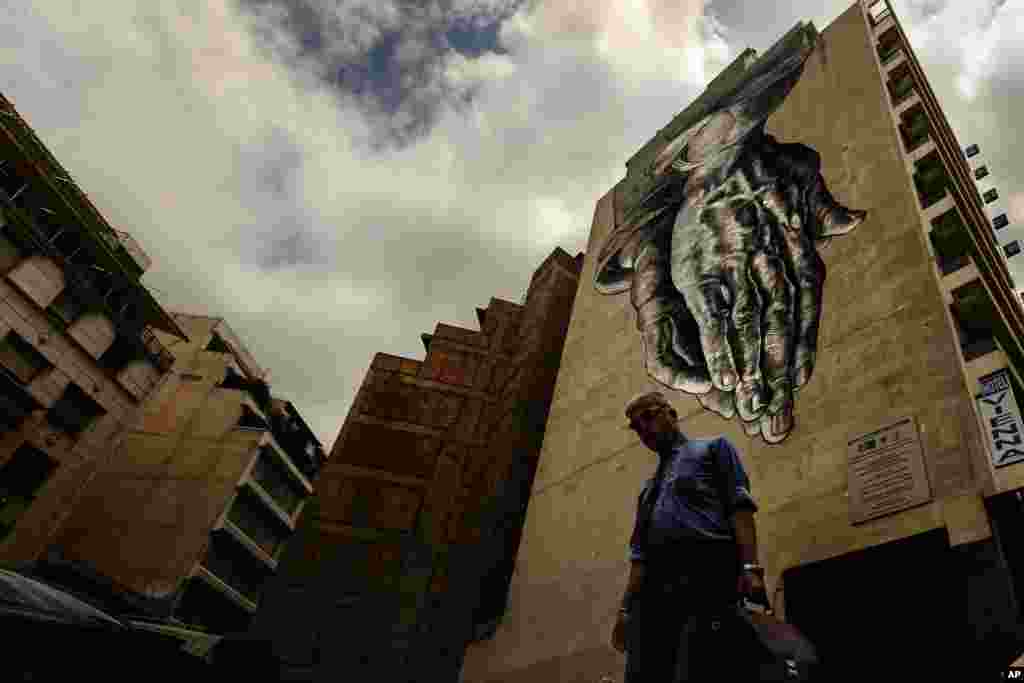 A man walks down a street with a turned upside-down mural inspired by "The Praying Hands" by Renaissance artist Albrecht Durer, in Athens. The bitter standoff between Greece and its international creditors was extended into the weekend, just days before Athens has to meet a crucial debt deadline.