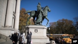 Visitors to the American Museum of Natural History in New York look at a statue of Theodore Roosevelt, flanked by a Native American man and African American man, Nov. 17, 2017.