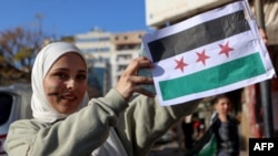 Seorang perempuan menunjukkan bendera oposisi Suriah di kota pesisir Latakia, pada 10 Desember 2024. (Foto: AFP/Aaref Watad)
