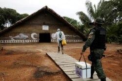 FILE - A municipal health worker and an environmental military police officer carry the AstraZeneca/Oxford vaccine as they enter an Indigenous hut at the Tupe Sustainable Development Reserve in Manaus, Brazil, Feb. 9, 2021.