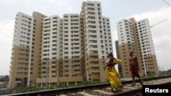 A woman carrying a child walks ahead of her husband on a railway track in front of residential buildings under construction on the outskirts of Kolkata, India, April 26, 2012.