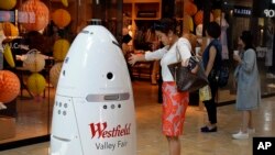 FILE - Sophie Li of Cupertino, California, offers to dance with a K5 robot made by Knightscope Inc., at Westfield Valley Fair shopping center in San Jose, California, June 26, 2017. 