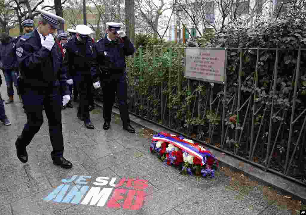 Policemen walk past spray painted on the sidewalk reading: &quot;Je suis Ahmed,&quot; or &quot;I am Ahmed,&quot; in the red, white and blue of the French flag near a plaque commemorating late police officer Ahmed Merabet in Paris, France. President Francois Hollande honored 17 victims killed in Islamic extremist attacks on satirical newspaper Charlie Hebdo, a kosher market and police a year ago this week.