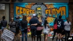 FILE - People are seen gathered at a memorial featuring a mural of George Floyd, near the spot where he died while in police custody, in Minneapolis, Minnesota, May 31, 2020.