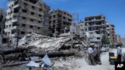 People stand in front of damaged buildings in the town of Douma, the site of a suspected chemical weapons attack, near Damascus, Syria, April 16, 2018. 