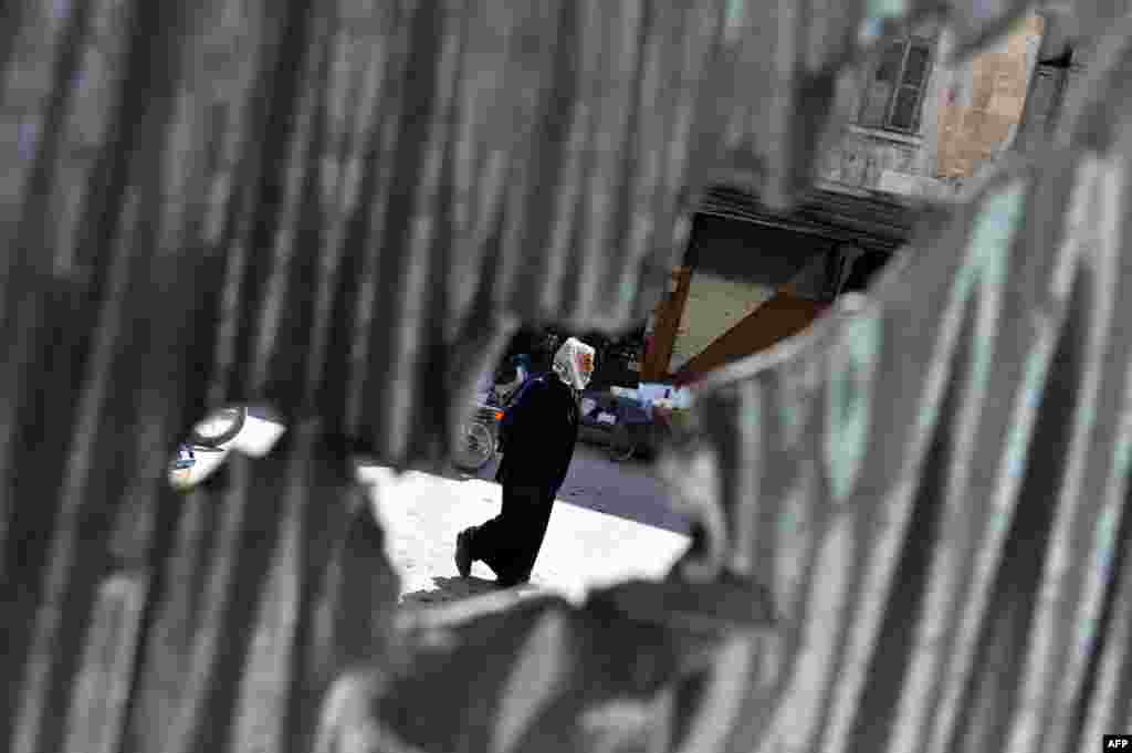 Seorang pria Suriah terlihat dari lubang sebuah pagar saat berjalan di kota Maarat al-Numan, provinsi Idlib, Suriah.