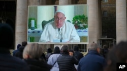 People look at a giant screen in St.Peter's Square, at the Vatican, showing Pope Francis reciting the Angelus noon prayer from his residence, after he decided not to appear at the window of his studio because of a persistent cold, Dec. 22, 2024.