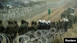 Polish soldiers and police watch migrants at the Poland/Belarus border near Kuznica, Poland, November 11, 2021, in this photograph released by the Territorial Defence Forces. 
