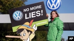 FILE - An activist from the environmental protection organization 'Greenpeace' holds a protest poster in front of a factory gate of German carmaker Volkswagen in Wolfsburg, Germany, Sept. 25, 2015. 