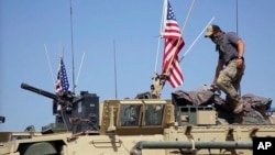FILE - This April 29, 2017, still taken from video, shows an American soldier standing on an armored vehicle in the northern village of Darbasiyah, Syria. 