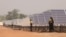 FILE - People stand next to solar panels of the solar energy power plant in Zagtouli, near Ouagadougou, Burkina Faso, Nov. 29, 2017, on its inauguration day.