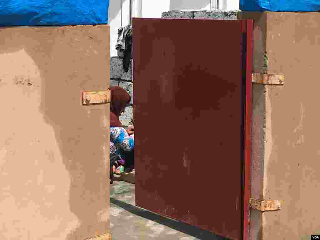 Iraqi woman who fled IS controlled village seen through the gate of a housing unit in a Kurdish-run camp for families fleeing IS control, outside Makhmour, Iraq, April 11, 2016. (S. Behn/VOA)