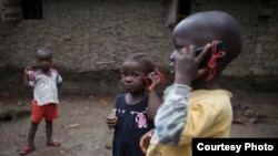 Olematu, 3, center, and Ibrahim, 4, talk on toy phones in a village near Kenema, Sierra Leone. Their 15-year-old sister, Betty, has taken charge after their mother’s death from Ebola. Betty survived an Ebola infection. (© UNICEF / Bindra) 