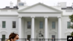 FILE - A woman wearing a face mask walks past the White House in Washington, April 1, 2020.