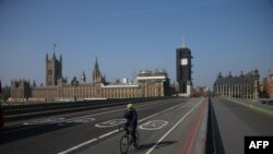 FILE - A cyclist crosses a near-empty Westminster Bridge with the Houses of Parliament in the background, amid the coronavirus outbreak, in central London, Britain, April 9, 2020.