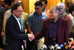FILE - Malaysian Prime Minister Mahathir Mohamad shakes hand with successor Anwar Ibrahim in Putrajaya, Feb. 22, 2020.