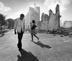 FILE - In this May 19, 1980, photo, people walk past ruins in Miami after rioting over the acquittal of four police officers charged with the 1979 beating death of a black man.