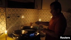 FILE - A man cooks near lit candles at his home during a power cut in San Cristobal, in the state of Tachira, Venezuela. Jorge Arreaza, Venezuela's science and technology minister, said the clock change will reduce the night-time use of lighting and air conditioning.
