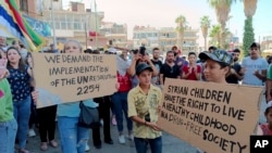 In this photo released by Suwayda24, people hold placards during a protest in the southern city of Sweida, Syria, Aug. 26, 2023. 