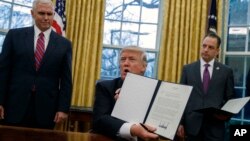 President Donald Trump shows off an executive order to withdraw the U.S. from the Trans-Pacific Partnership trade pact, Jan. 23, 2017, in the Oval Office of the White House in Washington.