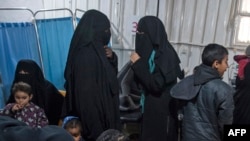 FILE - Two women, center, reportedly wives of Islamic State (IS) group fighters, wait with other women and children at a camp of al-Hol in al-Hasakeh governorate in northeastern Syria, Feb. 7, 2019.