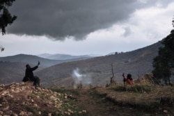 FILE - Displaced men look for a telephone signal among the ruins of houses destroyed by armed men near the internally displaced persons camp of Bijombo, South Kivu Province, eastern Democratic Republic of Congo, Oct. 11, 2020.