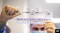 In this March 2021 photo provided by Pfizer, a technician inspects filled vials of the Pfizer-BioNTech COVID-19 vaccine at the company’s facility in Puurs, Belgium.