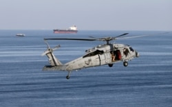 FILE - MH-60S helicopter hovers in the air with an oil tanker in the background as the USS John C. Stennis makes its way to the Gulf through the Strait of Hormuz, Dec. 21, 2018.