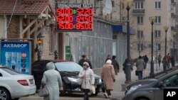 Orang-orang berjalan di bawah display informasi kurs Ruble Rusia yang terus menurun, di Moskow (1/12/2014). 