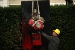 A bust of Belgium's King Leopold II is hoisted off of its plinth by a crane as it's removed from a park in Ghent, Belgium, June 30, 2020.