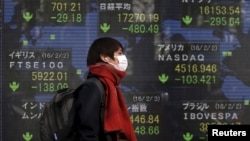 A pedestrian walks past an electronic board showing the stock market indices of various countries outside a brokerage in Tokyo, Japan, Feb. 3, 2016. 