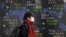 FILE - A pedestrian walks past an electronic board showing the stock market indices of various countries outside a brokerage in Tokyo, Japan, Feb. 3, 2016. 