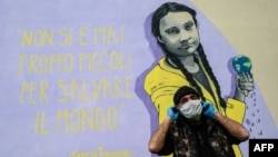 A resident wearing a face mask stands next to a mural featuring Swedish climate activist Greta Thunberg and her quote "You're never too young to save the world," in the Trullo district of Rome, March 30, 2020, during the COVID-19 pandemic.
