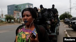FILE - A woman walks past Cameroonian elite Rapid Intervention Battalion (BIR) members as they sit on their military vehicle during their patrol in the city of Buea in the Anglophone southwest region, Cameroon, Oct. 4, 2018.