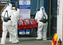 Medical workers wearing protective gear carry a patient infected with the COVID-19 coronavirus at a hospital in Chuncheon, Feb. 22, 2020.