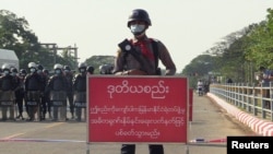 FILE - Policeman stands behind a banner reading "if this line is crossed, Myanmar police force will fire with live ammunition" during a protest against the military coup and to demand the release of Aung San Suu Kyi, in Naypyitaw, Myanmar, February 8, 2021.