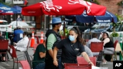 A waitress seats customers at a restaurant with outdoor dining on a section of street closed to traffic to promote social distancing, July 17, 2020, in Somerville, Mass.
