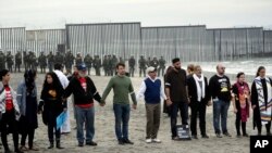 People hold hands in prayer during a protest in San Diego, near the border with Tijuana, Mexico, Dec. 10, 2018.