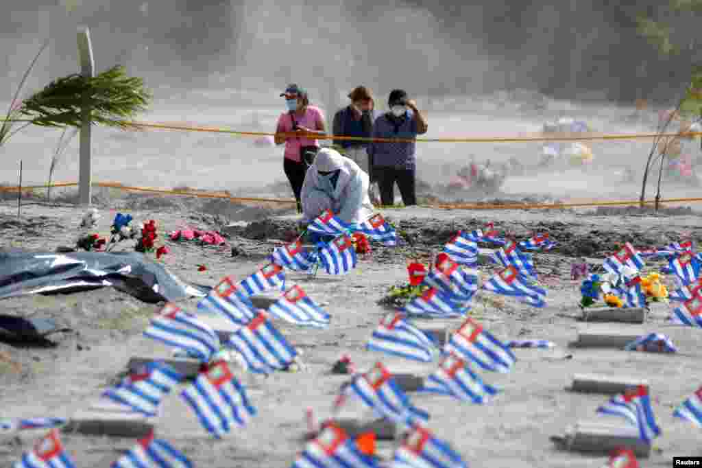 Un trabajador del Cementerio de la Bermeja en San Salvador, El Salvador, pone flores en la tumba de una persona que falleció de COVID-19.