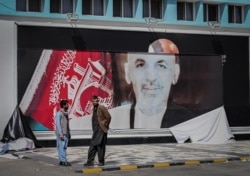 FILE - Afghan men stand next to a torn poster of Afghan President Ashraf Ghani at Kabul airport in Kabul, Aug. 16, 2021.