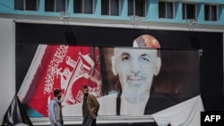 Afghan men stand next to a torn poster of Afghan President Ashraf Ghani at the Kabul airport in Kabul on August 16, 2021.