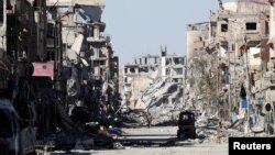 FILE - A fighter of the Syrian Democratic Forces stands amid the ruins of buildings near Clock Square in Raqqa, Syria, Oct. 18, 2017.