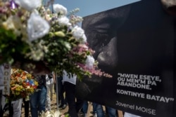 People place a portrait of slain Haitian President Jovenel Moise with a quote from him that reads in Creole "I try, you don't give up. Continue fighting," at a memorial outside the National Palace, in Port-au-Prince, Haiti, July 14, 2021.