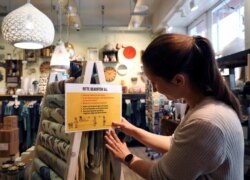 An employee places a sign with instructions about social distancing as she prepares to reopen a shop in the district of Prenzlauer Berg after a partial end of the lockdown in Berlin, April 18, 2020.