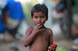 FILE - A child eats a pomegranate collected from waste at a slum area on the outskirts of Jammu, India, Oct. 12, 2018.